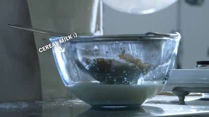 Cornflake milk being strained into a large mixing bowl using a household strainer.