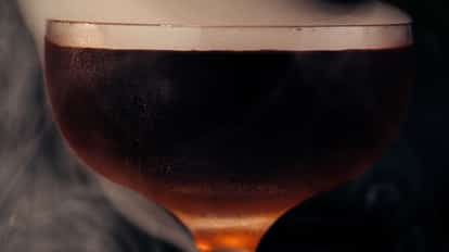 A Manhattan cocktail enveloped in smoke from a smoking gun adding flavor and aroma.