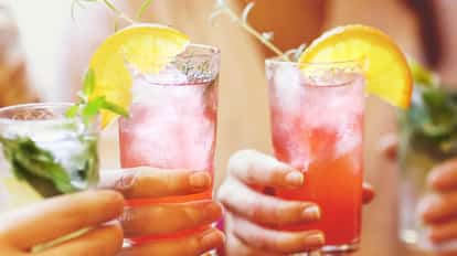 Mocktails iced in tall glasses with orange wedges and herb sprigs