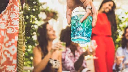 Blue cocktail in a patterned rocks glass held in a group at an outdoor party.