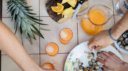 Three orange drinks with ice and a pitcher, pineapple, a plate of clams and an Absolut bottle at the edge