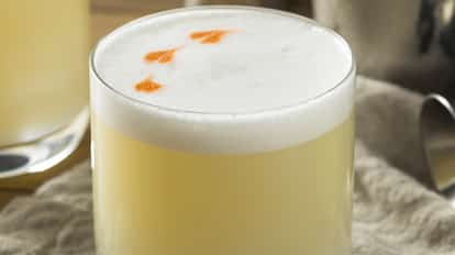 A foam-topped sour cocktail in a rocks glass with three orange bitters dots.