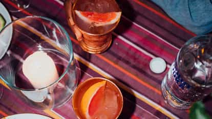 Two mule cocktails in copper mugs garnished with grapefruit wedges, one mug held by a hand on a striped tablecloth.