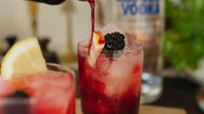 Cocktail in a rocks glass with ice, blackberry and lemon wedge and an Absolut Vodka bottle in the background