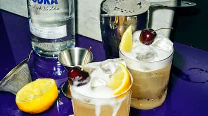 Two Vodka Cocktail cocktails garnished with a maraschino cheery and lemon wedge, next to a bottle of Absolut Vodka.