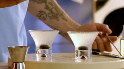 Garnishing two cocktails glasses with Marschino cherries