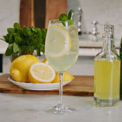 Limoncello Spritz in a wine glass next to a bottle of Limoncello, Prosecco and sofa water.