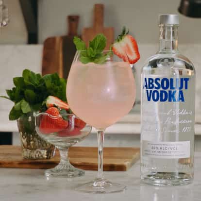 Rhubarb Spritz cocktail in a wine glass garnished with a strawberry and a mint sprig next to a bottle of Absolut Vodka.