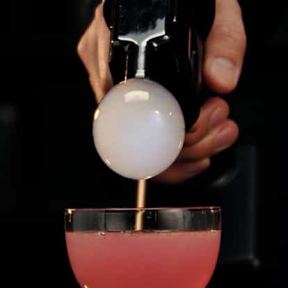 Cocktail bubble gun releasing a bubble on top of a Cosmopolitan cocktail.