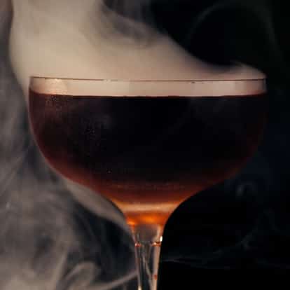 A Manhattan cocktail enveloped in smoke from a smoking gun adding flavor and aroma.