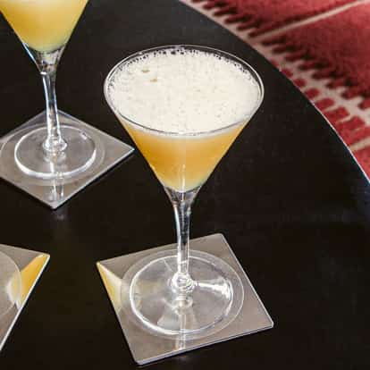 Absolutely Bananas Cocktails in gekühlten Martinigläsern mit leichter Schaumkrone, serviert auf einem dunklen Tisch mit klaren quadratischen Untersetzern.