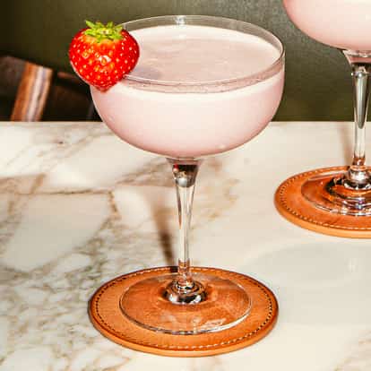 Dwa eleganckie martini Black Forest Gateau w kieliszkach coupe z jasnoróżową pianką, udekorowane świeżą truskawką na marmurowym stole.