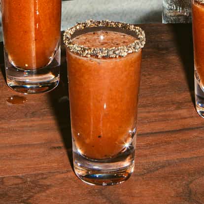 Bloody Mary Shot im klaren Glas mit Pfefferrand auf Holztisch, kräftige Tomatenfarbe und glatte Textur.