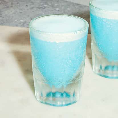 Zwei frostige Gläser des Blue Jay Cocktails, hellblau und schaumig, kalt serviert auf einer Steinoberfläche.