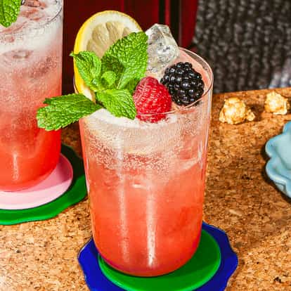 Zwei Campari-Nobile-Cocktails mit Eis, Himbeeren, Brombeeren, Zitronenscheiben und frischer Minze in hohen Gläsern auf bunten Untersetzern.