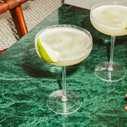 Elderflower Pear Martinis in coupe glasses garnished with fresh pear slices on a green marble table.