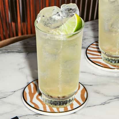 Firework-Drink in hohen, eisgefüllten Gläsern mit Limettenstücken auf gemusterten Untersetzern auf einem weißen Marmortisch.