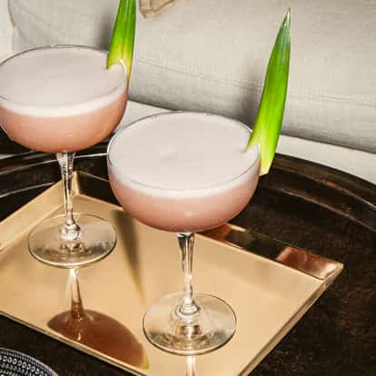 Zwei French-Martini-Cocktails in rosafarbenen Coupégläsern mit Schaumkrone und Ananasblättern, serviert auf einem goldenen Tablett im modernen Lounge-Ambiente.