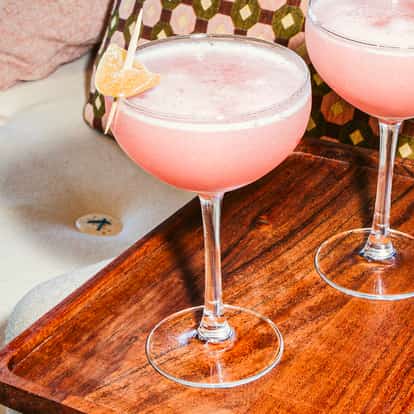 Ginger Cosmos in Coupette-Gläsern mit kandiertem Ingwer auf einem Holztablett über einem hellen Sofa.