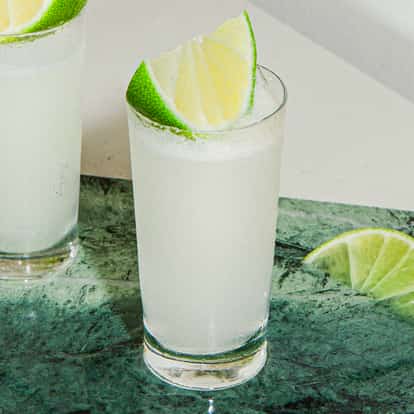 Dos cócteles Kamekaazi en vasitos tipo shot helados con gajos de lima, servidos sobre una tabla de piedra verde en un ambiente moderno y luminoso.