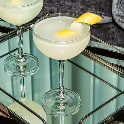 Lemon Martinis in Coupette-Gläsern mit frischer Zitronenschale auf einem Spiegeltablett über Metalloberfläche.