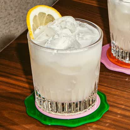 Cocktail Loneiless in bicchiere basso con ghiaccio e fetta di limone, drink chiaro e opaco su tavolo in legno.