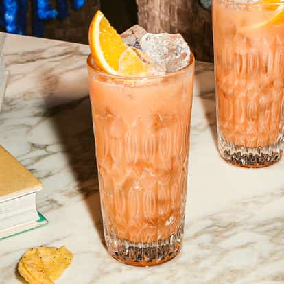 Madras Cocktail in hohen gemusterten Gläsern mit Eis und Orangenspalte, rosa Zitrusdrink auf Marmortisch mit Büchern.