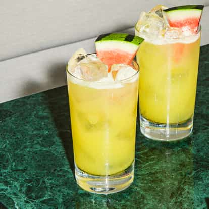 Melon Ball Cocktails in Highball-Gläsern mit frischen Wassermelonenscheiben auf grüner Marmoroberfläche.