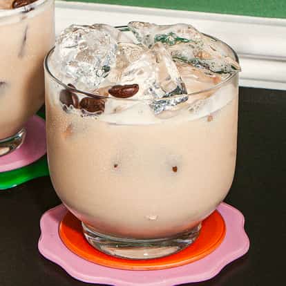 Muddy-Water-Cocktails in runden, gekühlten Gläsern mit Eis und Kaffeebohnen als Deko, auf bunten Untersetzern auf einer dunklen Tischplatte.