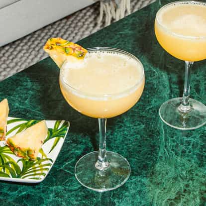 Cócteles Pineapple Martini en copas coupé, con espuma de piña y trozos frescos, servidos sobre una mesa de mármol verde.