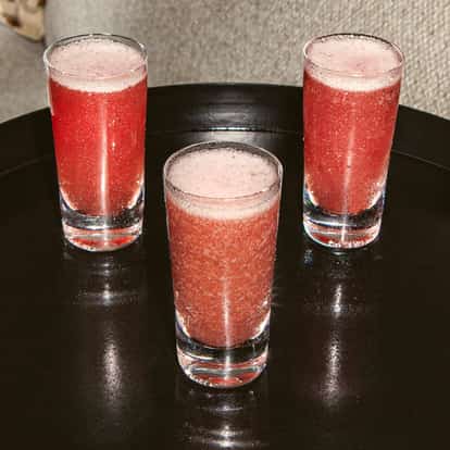 Drei Purple Haze Shots in klaren Shotgläsern mit schaumiger pink-violetter Mischung auf einem glänzenden schwarzen Tablett.