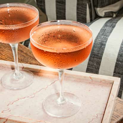 Quattro Bianchi Cocktails in gekühlten Coupégläsern, serviert auf einem rosafarbenen Marmortablett neben Snacks.