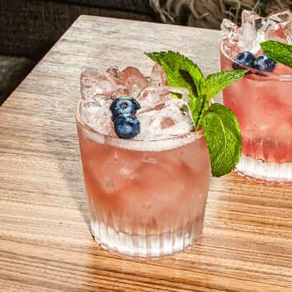Razzle-Dazzle-Cocktails in gekühlten Gläsern, voller Eis und garniert mit frischen Blaubeeren und Minze, serviert auf einem Holztisch.