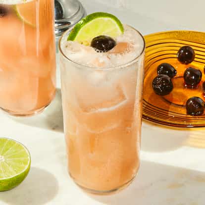 Two Sex on the Beach cocktails with ice, lime slices, and cherries on a marble surface beside an amber plate filled with dark cherries.