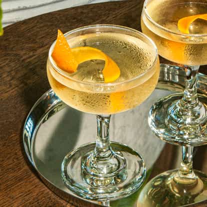 Soho Martini Cocktails in gekühlten Coupégläsern mit Zitruszesten, serviert auf einem silbernen Tablett auf einem Holztisch.