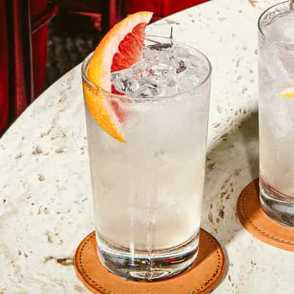 Summertime Cocktail im hohen Glas mit Eis und frischer Grapefruitscheibe, klarer erfrischender Drink auf Steintisch.