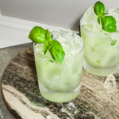 Vodka Basil Smash cocktails in frosty glasses with fresh basil leaves and ice on a round stone tray.