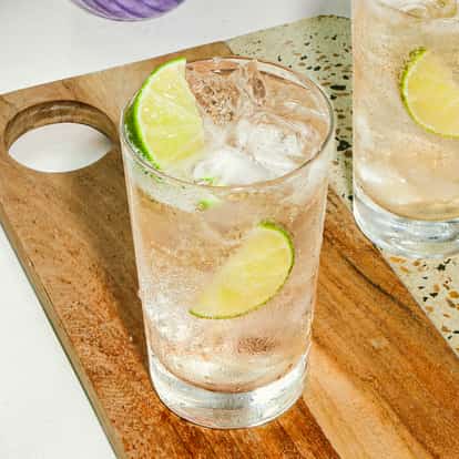 Vodka-Ginger-Ale-Cocktails, serviert in hohen, gekühlten Gläsern mit Eis und frischen Limettenscheiben, auf einem Holzbrett angerichtet.