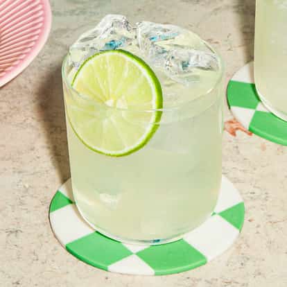 A Vodka Lime cocktail in a short glass with ice and a lime wheel, standing on a green-and-white checkered coaster on a stone countertop.