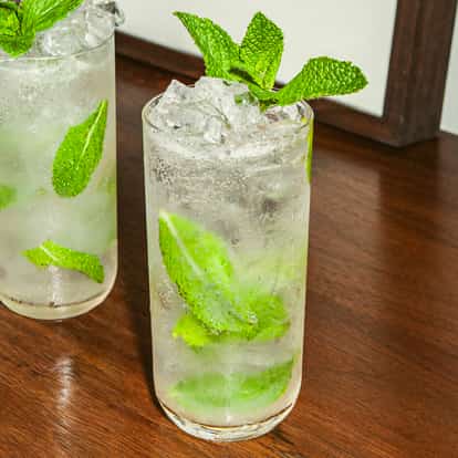 Dois coquetéis vodka mojito com hortelã fresca e gelo picado em copos altos sobre superfície de madeira.