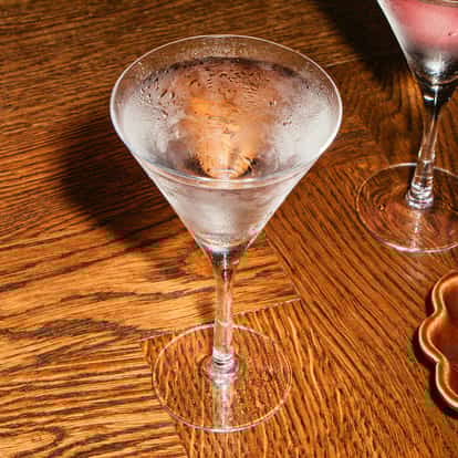 Vodka-Stinger-Cocktails in gekühlten Martinigläsern mit frostigem Schimmer, serviert auf einem Holztisch neben einer kleinen Schale Snacks.