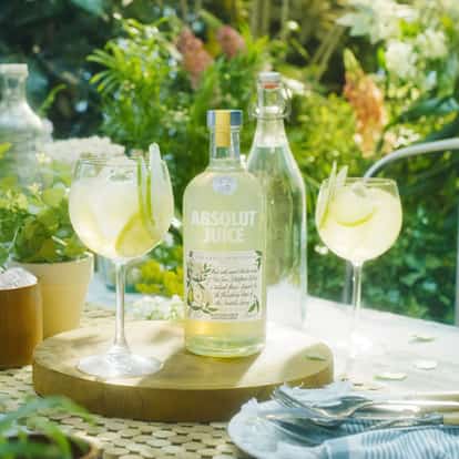 Absolut Juice Pear and Elderflower bottle on a wooden board with two stemmed glasses with ice and pear slices