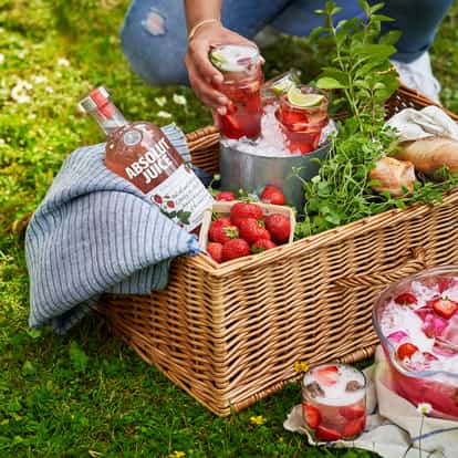 Absolut Juice Strawberry bottle in a picnic basket beside an ice bucket holding two iced glasses garnished with lime