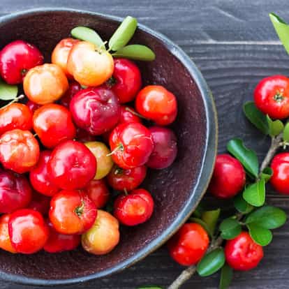 Acerola in a ceramic bowl with stems and leaves on a wooden surface