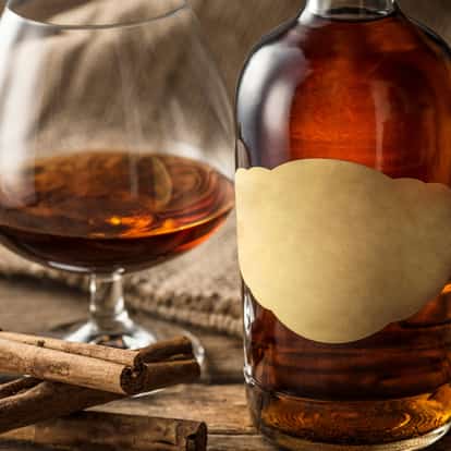 Martinique Rum in a snifter with cinnamon sticks and a nearby unlabeled bottle on wooden surface