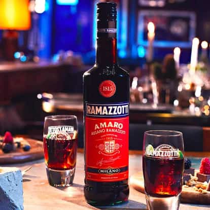 Amaro Ramazzotti bottle on a table with two glasses filled with liqueur and plates and candles in background