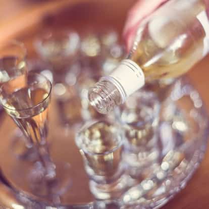 Aquavit bottle pouring into multiple shot glasses on a round tray