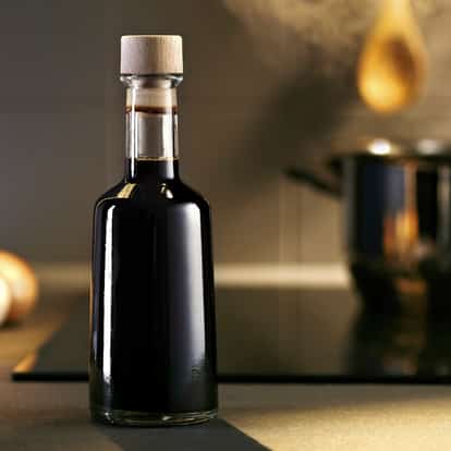 Balsamico vinegar in a tall glass bottle with wooden stopper on a stovetop