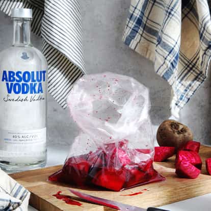 Beet Infused Vodka with chopped beets in a plastic bag on a wooden board and an Absolut vodka bottle