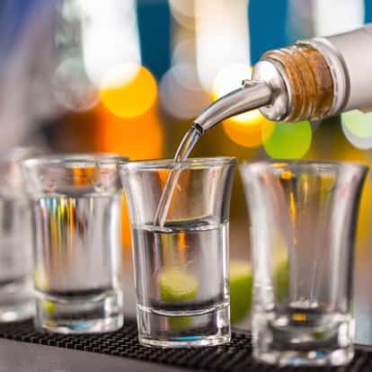 Bison Grass Flavored Vodka in a shot glass with a bottle pourer filling it and two shot glasses beside